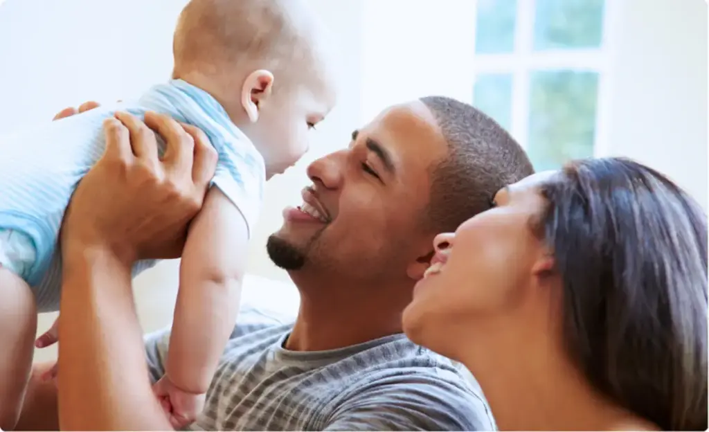 Parents smile as they hold and play with their baby in a bright home setting.